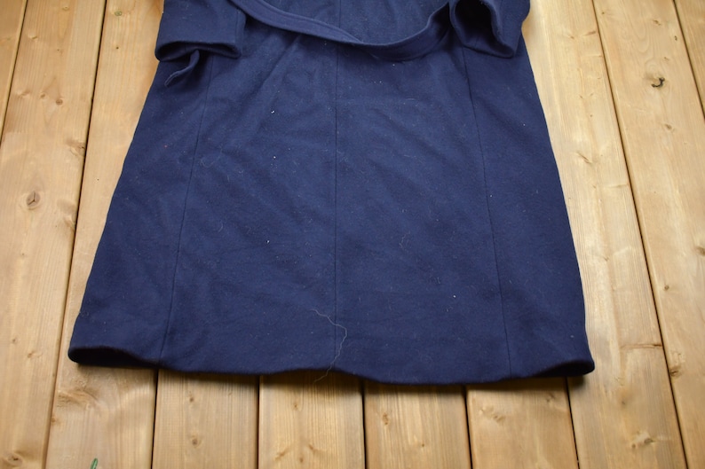 Pu&ograve; includere: Una vestaglia blu navy con cintura.