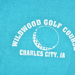 May include: Teal-colored fabric with a white graphic. The graphic features the words "Wildwood Golf Course" in an arch, with a golf ball design in the center. Below, the text reads "Charles City, IA."