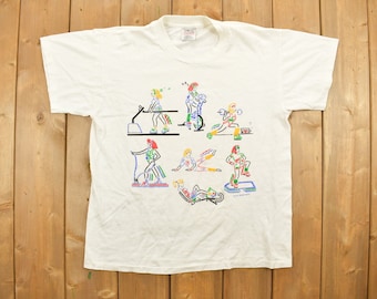 Puede incluir: Camiseta blanca con un gráfico colorido de personas haciendo ejercicio en diferentes equipos de fitness. El gráfico incluye una cinta de correr, una bicicleta estática, pesas y otras máquinas de ejercicio.