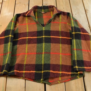 May include: A vintage plaid shirt in shades of brown, green, black, red, and yellow. The shirt features a V-neck collar and a classic plaid pattern. The fabric appears to be a soft, woven material, perfect for cooler weather.