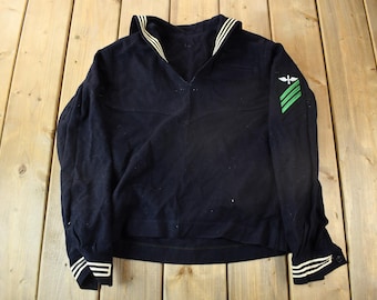 May include: A dark blue sailor shirt with a white collar and cuffs. The shirt has a green and white patch on the right sleeve.