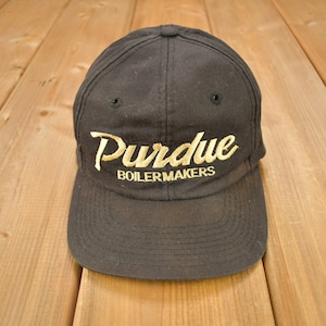 Może przedstawiać: Czarna czapka bejsbolówka z haftowanym złotym logo z napisem "Purdue Boilermakers".