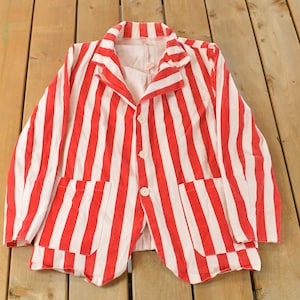 May include: A red and white striped blazer with two front pockets and three white buttons. The jacket is laid flat on a wooden surface. The blazer has a classic, casual style.