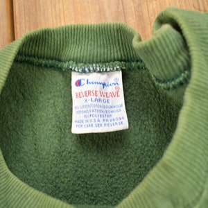 May include: Green Champion Reverse Weave sweatshirt with a white tag that reads "Champion Reverse Weave X-Large 90% Cotton/Coton/Baumwolle Cotone/Katoen/Bomuld 10% Polyester Made in USA RH 26094 For Care See Reverse"