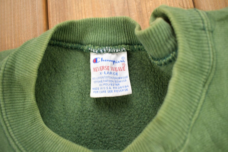 May include: Green Champion Reverse Weave sweatshirt with a white tag that reads "Champion Reverse Weave X-Large 90% Cotton/Coton/Baumwolle Cotone/Katoen/Bomuld 10% Polyester Made in USA RH 26094 For Care See Reverse"