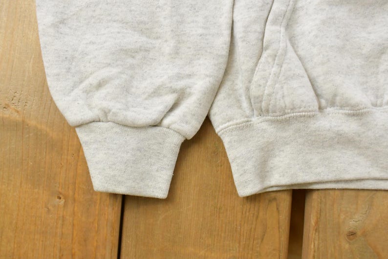 Op de afbeelding: Een lichtgrijs gem&ecirc;leerd sweatshirt met lange mouwen en geribbelde boorden. Het kledingstuk heeft een gestructureerd, gespikkeld stofpatroon over het geheel, met zichtbare stikdetails langs de mouwnaden en een deel van de voorzak.