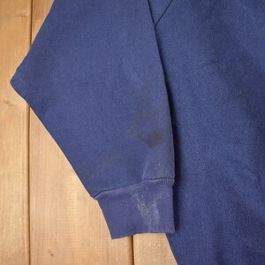 May include: A dark blue sweatshirt with a long sleeve. The sleeve has a dark stain on it.