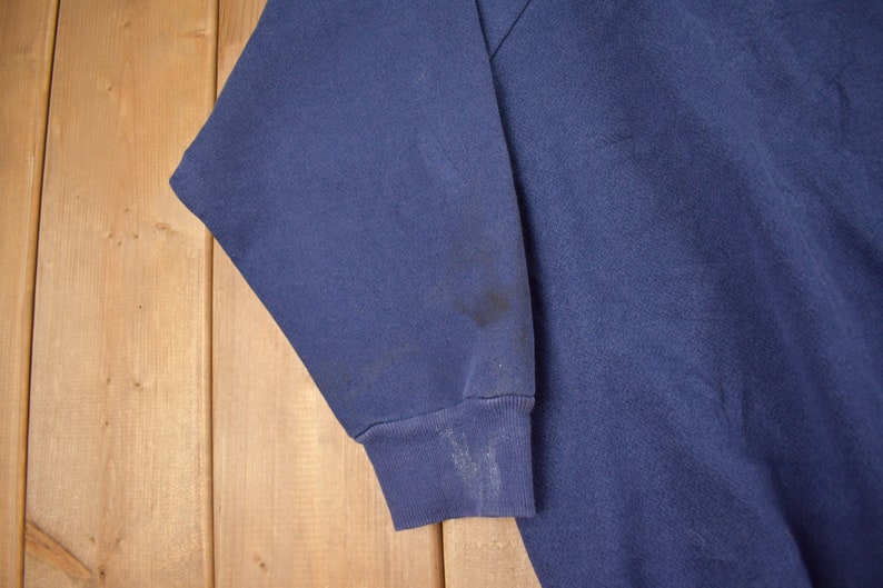 May include: A dark blue sweatshirt with a long sleeve. The sleeve has a dark stain on it.