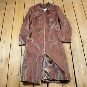 May include: A long brown leather coat with a zip closure. The coat has a collar and two pockets.