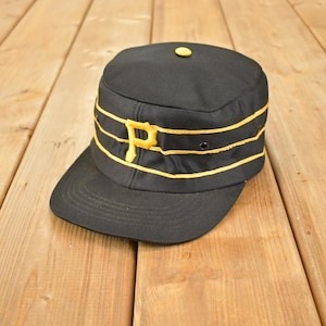 May include: Black baseball cap with a flat peak and a yellow "P" logo. The cap has yellow stripes and a yellow button on top. The hat is made of a durable fabric, possibly vintage.
