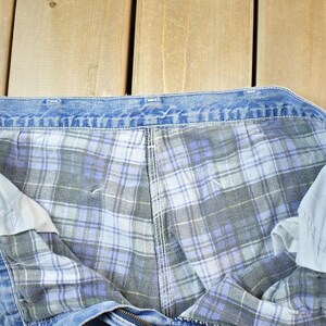 K&ouml;nnte beinhalten: Nahaufnahme einer blauen Jeans-Arbeitshose mit einem karierten Flanellfutter in Blau-, Grau- und Wei&szlig;t&ouml;nen. Die Hose liegt flach, wobei das Innenfutter und das Jeans-Au&szlig;enmaterial zu sehen sind.