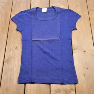 Puede incluir: Una camiseta azul lisa de cuello redondo.