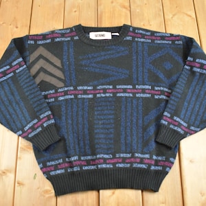 May include: A vintage black sweater with a geometric pattern in blue, brown, and purple. The sweater has a crew neck and long sleeves. The brand name "GITANO" is on a tag at the neckline. The sweater is made of a soft, knit material.