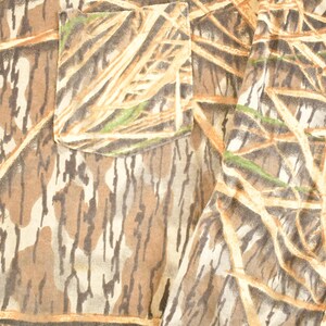 May include: Long-sleeved shirt with a camouflage pattern in shades of brown, tan, and green. The shirt features a chest pocket and a naturalistic design, suitable for outdoor activities.