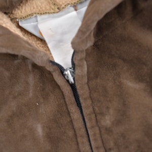 May include: Close-up of a brown hooded sweatshirt with a zipper. The zipper is black and has a silver pull tab.