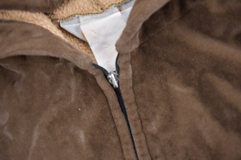 May include: Close-up of a brown hooded sweatshirt with a zipper. The zipper is black and has a silver pull tab.