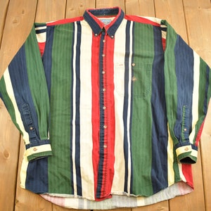 Puede incluir: Una camisa de manga larga con botones y rayas verticales en tonos de azul, verde, rojo y blanco.