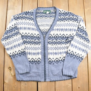 Könnte beinhalten: Ein blauer und weißer gemusterter Cardigan mit Reißverschluss. Der Cardigan hat ein Fair Isle-Muster mit einem geometrischen Muster.