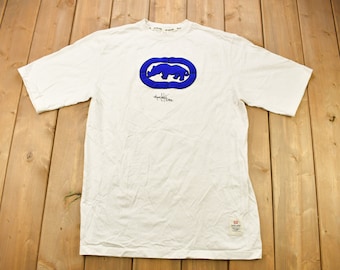 May include: White t-shirt with a blue rhinoceros logo and the text "State Property" printed on the front.