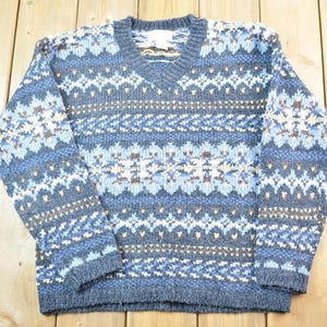 Può includere: Un maglione di lana blu, bianco e marrone con scollo a V.