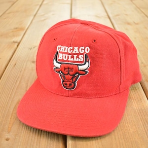 Puede incluir: Gorra de béisbol roja con el logotipo de los Chicago Bulls. El logotipo presenta la cabeza de un toro con cuernos blancos y el nombre del equipo en letras blancas. La gorra está hecha de tela resistente y tiene una visera curva.