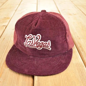 May include: Maroon corduroy trucker hat with the embroidered text "Las Vegas" in white script. The hat features a mesh back and a curved brim. A classic accessory for casual wear.