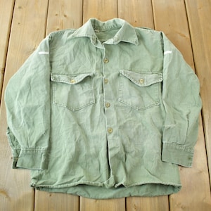May include: A green long-sleeved shirt with a button-up front and two chest pockets. The shirt has white stitching on the sleeves.