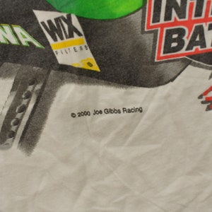 May include: White t-shirt featuring a black and green graphic of a car with the text "MBNA", "WIX Filters", "Interstate Batteries", and "Racing". The text "&copy; 2000 Joe Gibbs Racing" is printed at the bottom of the shirt.