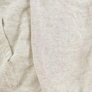 Op de afbeelding: Een lichtgrijs gem&ecirc;leerd sweatshirt met een zachte, gespikkelde textuur. Het kledingstuk is voorzien van een zichtbare voorzak met gestikte naden, wat het gebreide materiaal en het subtiele gevlekte patroon van de stof benadrukt.