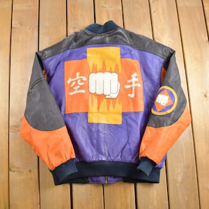 May include: A black, orange, and purple leather bomber jacket with a large graphic on the back. The graphic features a fist in flames with Japanese characters that read "空手" (karate).