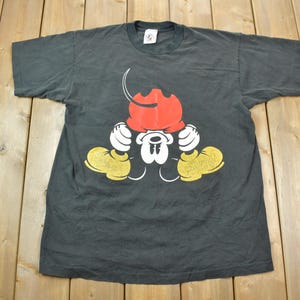 May include: Black t-shirt with a graphic of Mickey Mouse in a red hat and yellow shoes. The graphic shows Mickey Mouse with his hands on his head, looking down.