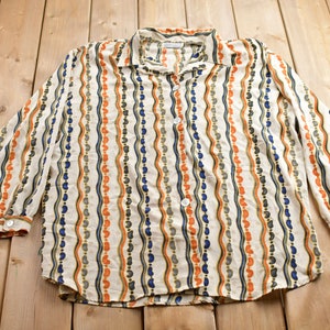 May include: A long-sleeved button-up shirt with a white background and a colourful pattern of stripes and wavy lines. The pattern features shades of blue, orange, and green.
