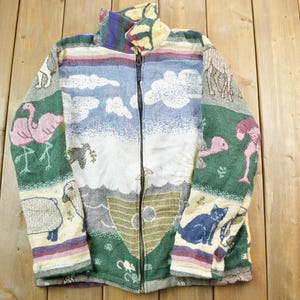 Peut inclure: Une veste zippée colorée avec un motif de tapisserie tissée représentant des animaux, des nuages et un bateau. La veste est de couleur verte, bleue, rose et blanche.