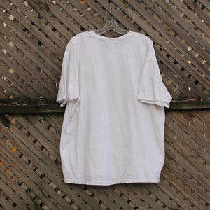 May include: A plain white t-shirt hanging on a wooden slatted fence.
