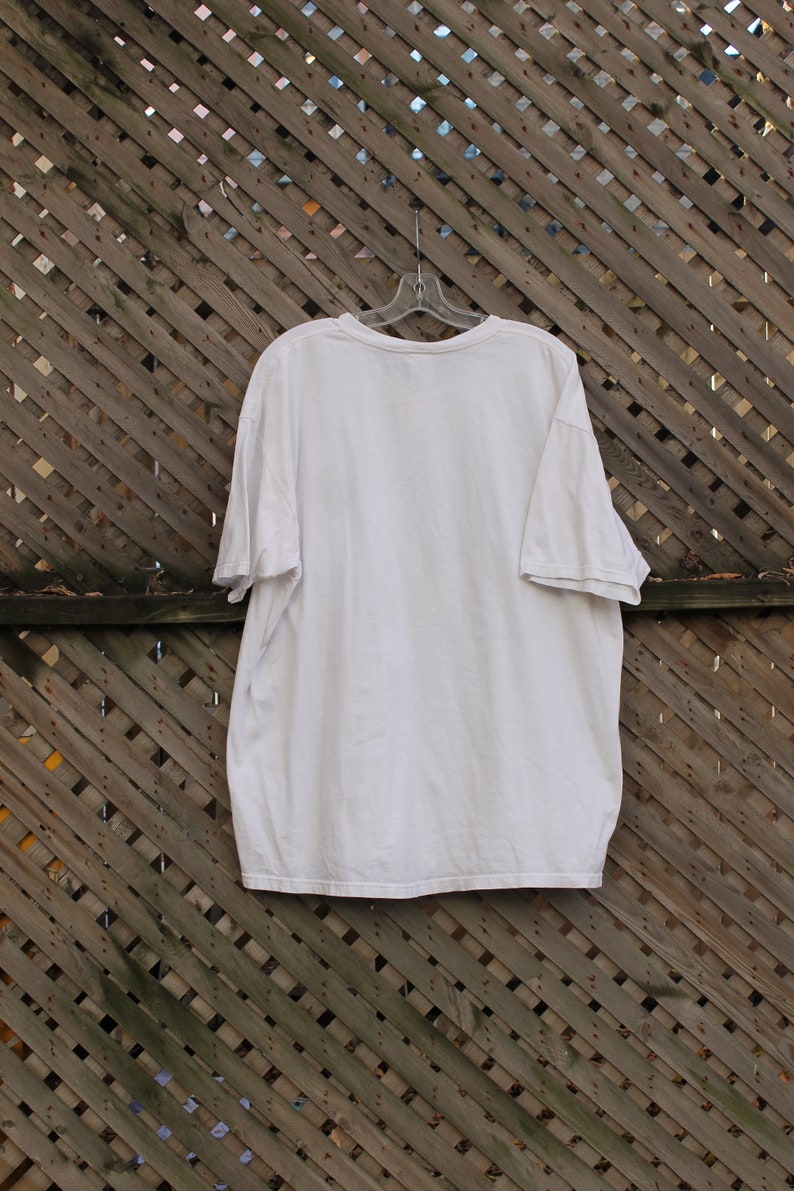 May include: A plain white t-shirt hanging on a wooden slatted fence.
