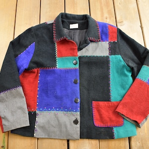 May include: A black, red, blue and green patchwork jacket with a button fastening and a pocket on the front.