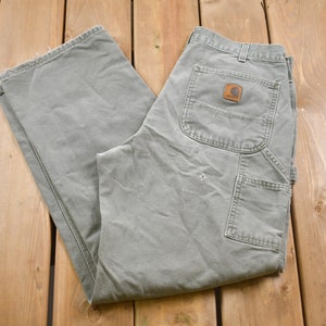 May include: A pair of grey work trousers with a brown Carhartt logo patch on the back pocket.