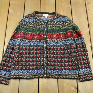 May include: A vintage button-up cardigan sweater with a colorful pattern. The sweater features a black base with red, blue, green, and gold floral and geometric designs. The sweater has a round neckline and long sleeves.