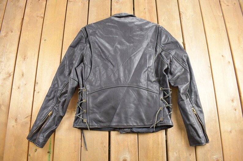 May include: Black leather jacket with a lace-up detail on the sides. The jacket has a zipper on the front and on the sleeves.