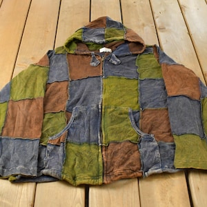 Könnte beinhalten: Ein langärmeliger Kapuzenpullover mit Reißverschluss und Patchwork-Design, bestehend aus quadratischen Stoffbahnen in Olivgrün, Schieferblau und Erdbraun. Das Kleidungsstück verfügt über eine Kapuze mit Kordelzug und zwei Vordertaschen.