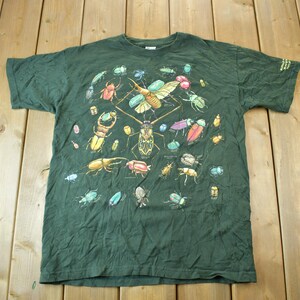 Pode incluir: Uma camiseta verde escura com uma estampa colorida de vários insetos, incluindo besouros, borboletas e mariposas.