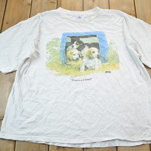 May include: White t-shirt featuring a graphic of three puppies peeking out of a dog house. The text "There's a Crowd" is printed below the image.