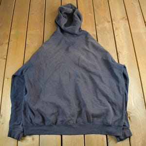 K&ouml;nnte beinhalten: Ein dunkelgrauer Kapuzenpullover mit langen &Auml;rmeln, flach auf einer Holzoberfl&auml;che liegend. Der Hoodie hat eine Kapuze mit Kordelzug und gerippte S&auml;ume und B&uuml;ndchen. Der Pullover ist einfarbig und aus weichem Material.