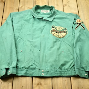 Op de afbeelding: Een groene vintage baseballjas met een patch op de linkerborst met de tekst "Ottawa Sr.  Senators 1960" en een patch op de rechtermouw met de tekst "16".