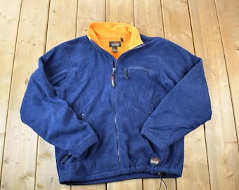 May include: A navy blue fleece jacket with a full zipper and an orange collar. The jacket has two zippered pockets and a drawstring at the bottom. The L.L.Bean logo is visible on the collar.