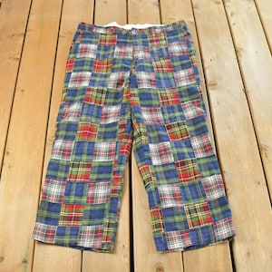 Könnte beinhalten: Patchwork-Hose mit Karomuster in Blau-, Grün-, Rot- und Weißtönen. Die Hose hat ein Patchwork-Design mit verschiedenen Karomustern. Die Hose liegt auf einer Holzoberfläche.