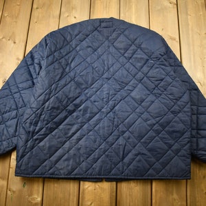 May include: A navy blue quilted jacket with a diamond pattern. The jacket has a zipper closure and a stand-up collar.