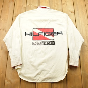 May include: White long-sleeved button-down shirt with a red and white scuba diving flag graphic and the text "HILFIGER AQUATIC SPORTS" on the back.