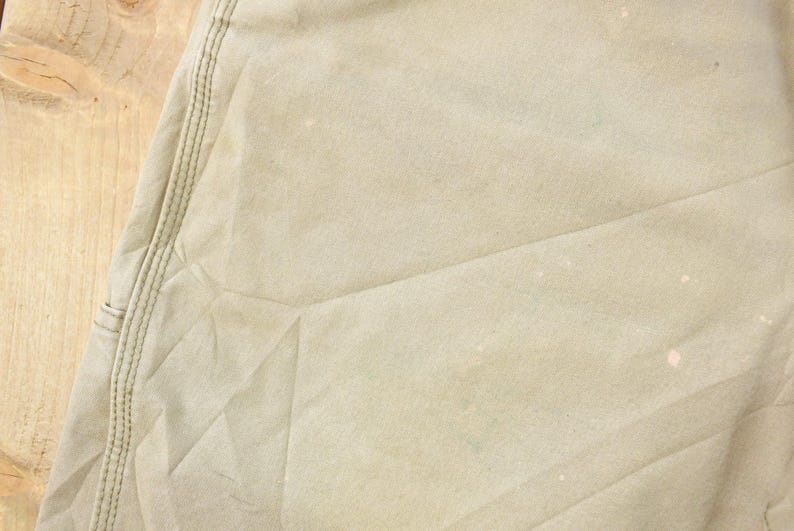 May include: Close-up of a section of tan fabric, possibly canvas or a similar material. Visible are seams with stitching, and the fabric has a slightly worn appearance with some light-colored spots.