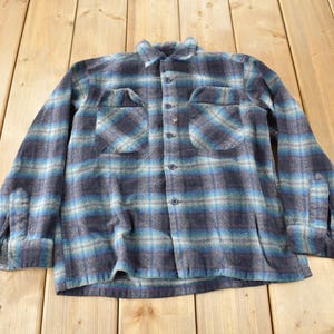 以下が含まれることがあります： 長袖で胸にポケットが2つ付いた、青と茶色の格子柄のフランネルシャツです。